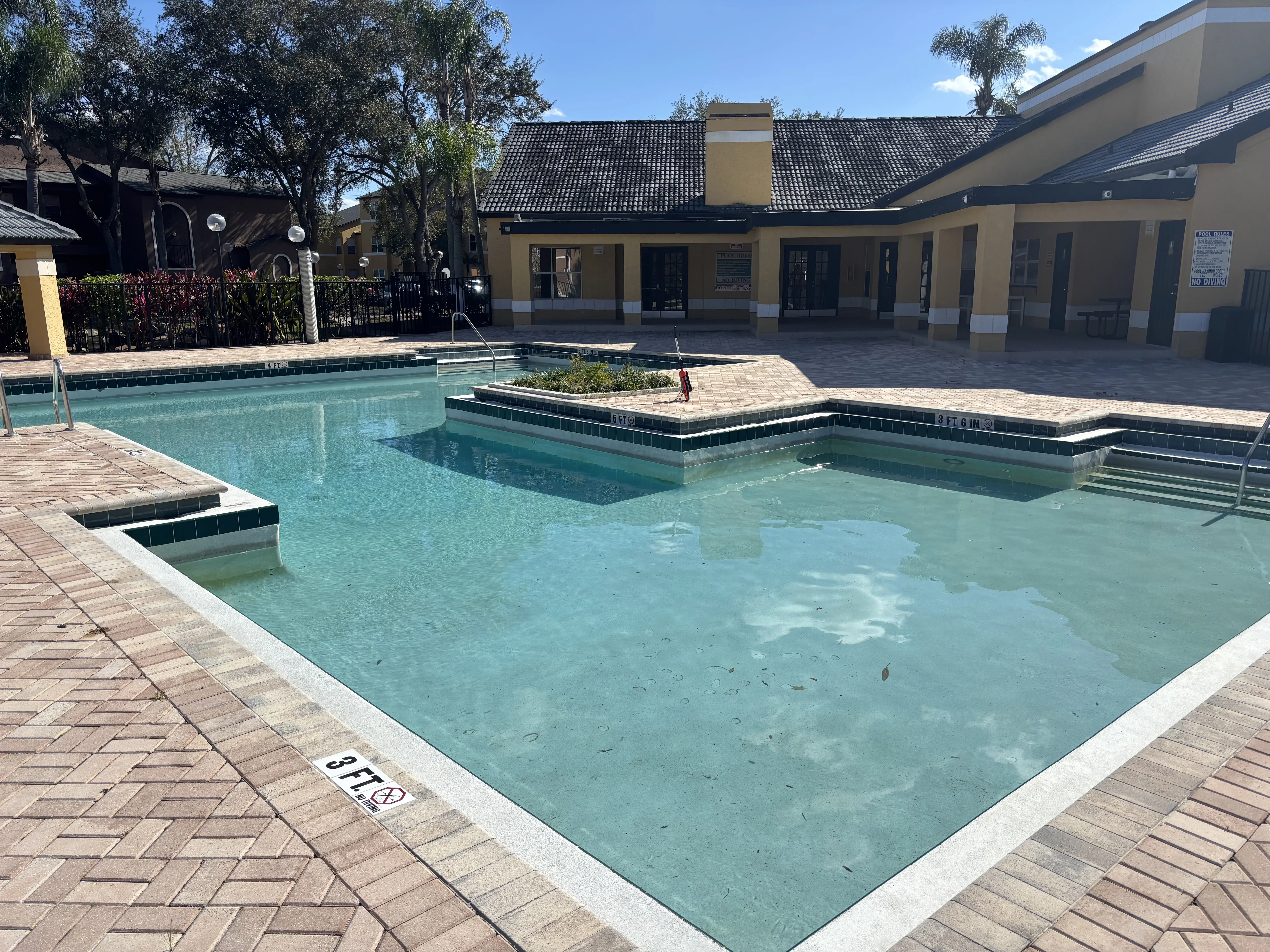Large community pool with clear water, dark tile trim, multiple connected pools, and paver deck