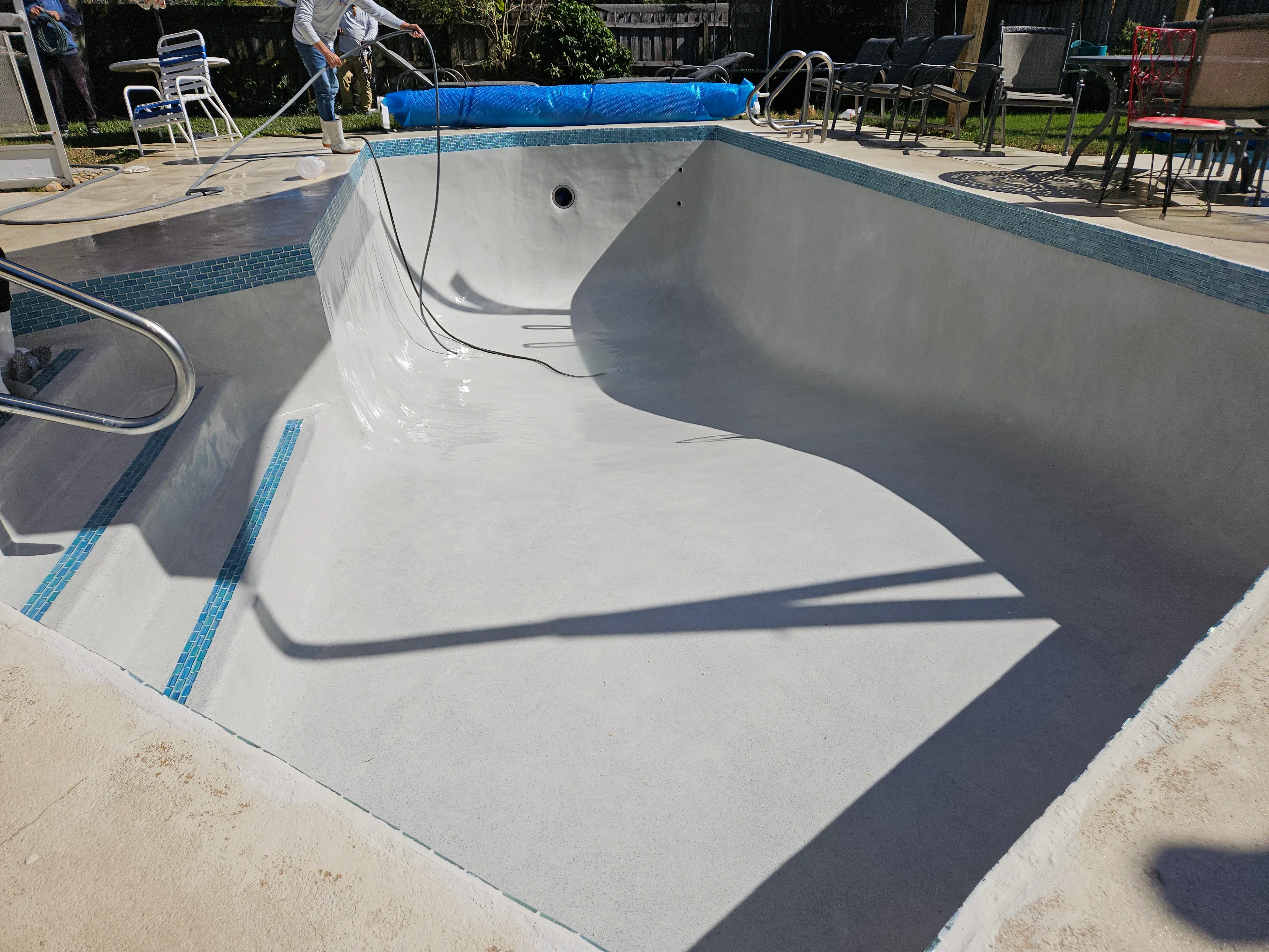 Newly resurfaced pool with white plaster finish and blue glass tile waterline detail