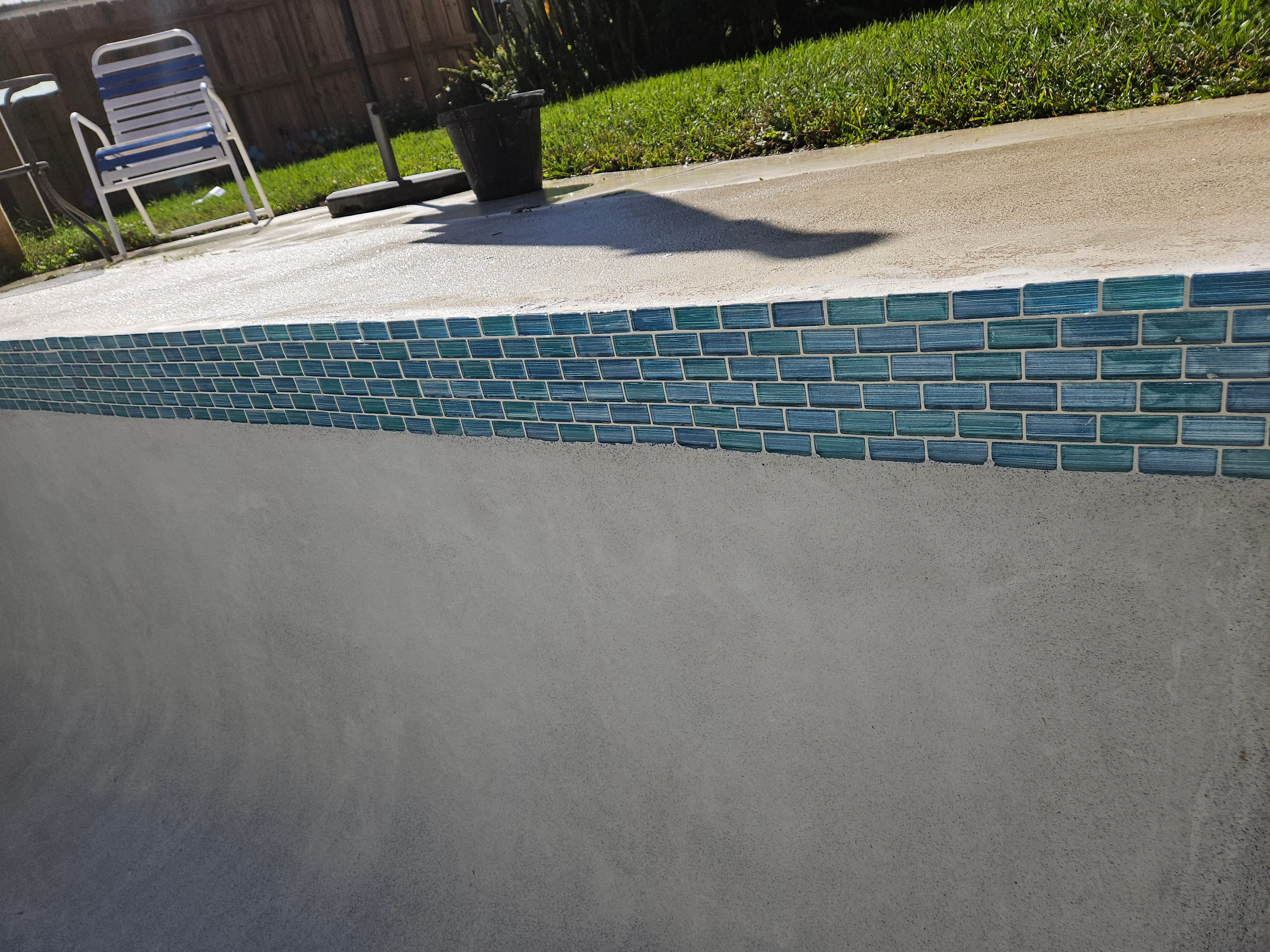 Teal glass tile waterline installation on pool with concrete deck and grouted joints