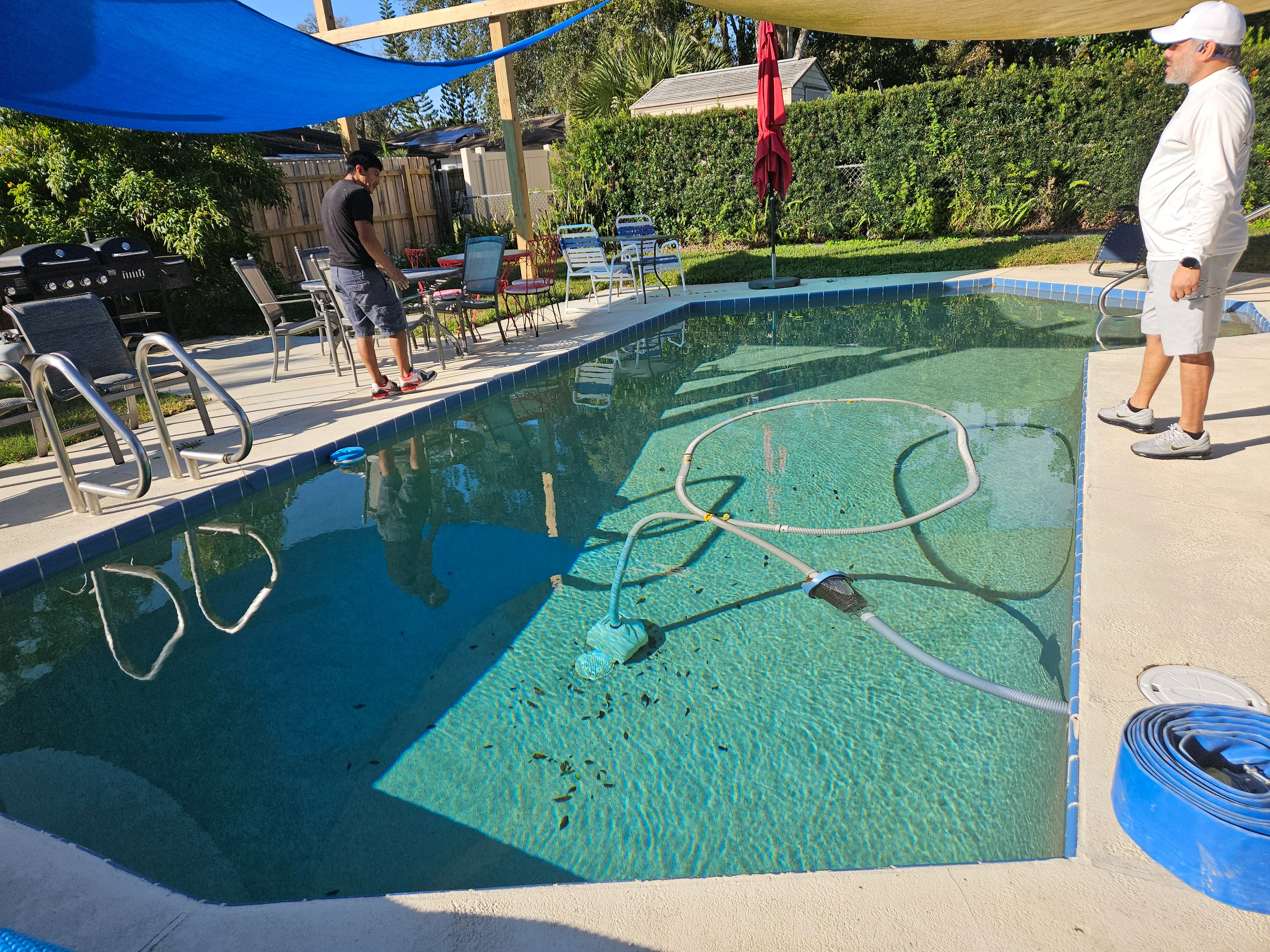 Technician cleaning residential pool with green plaster finish, tile border, and maintenance equipment