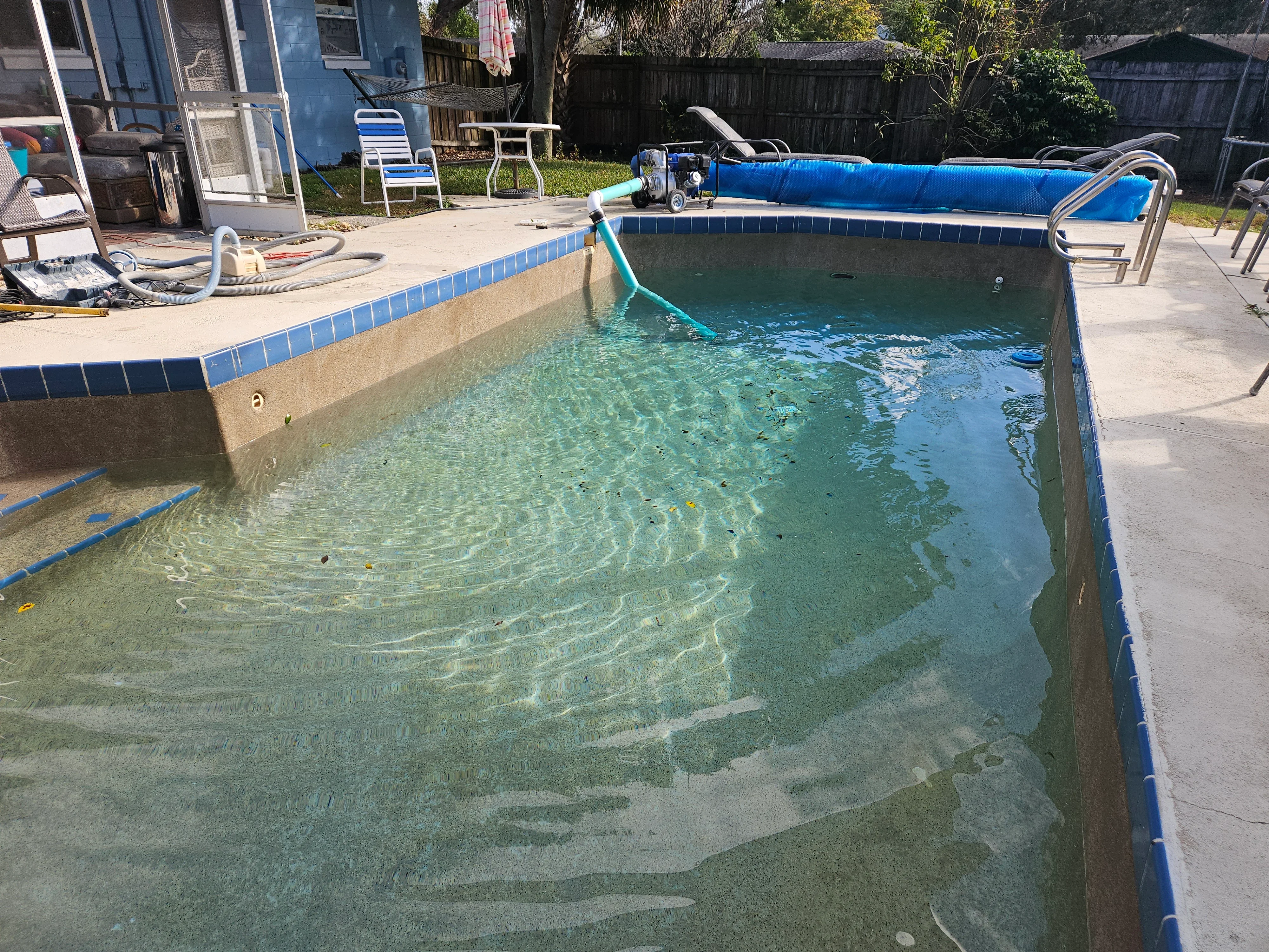 In-ground pool with blue tile trim during cleaning and water treatment, showing circulation equipment and concrete deck