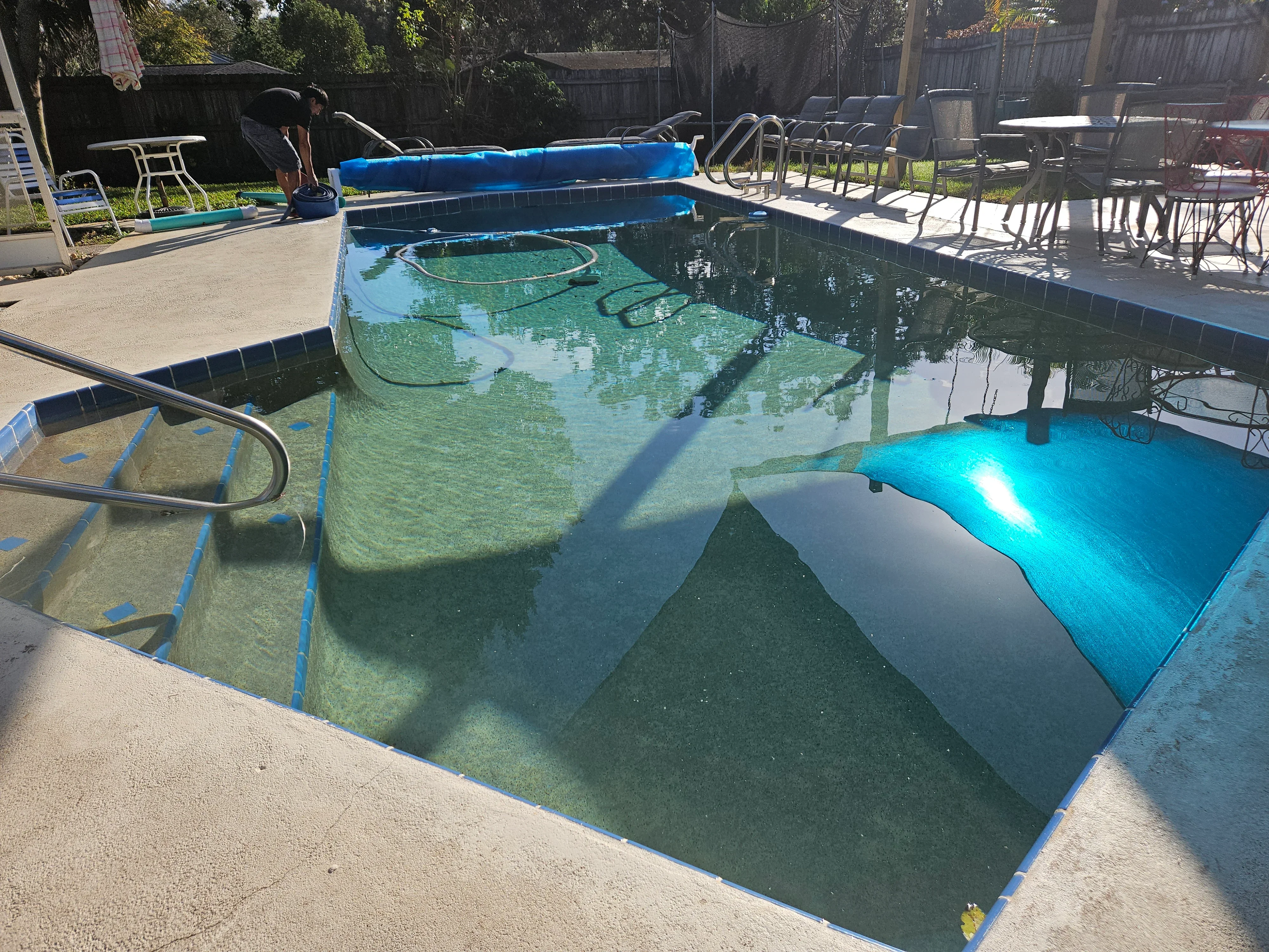 In-ground pool with blue vinyl liner being cleaned and treated, showing algae removal and water circulation equipment