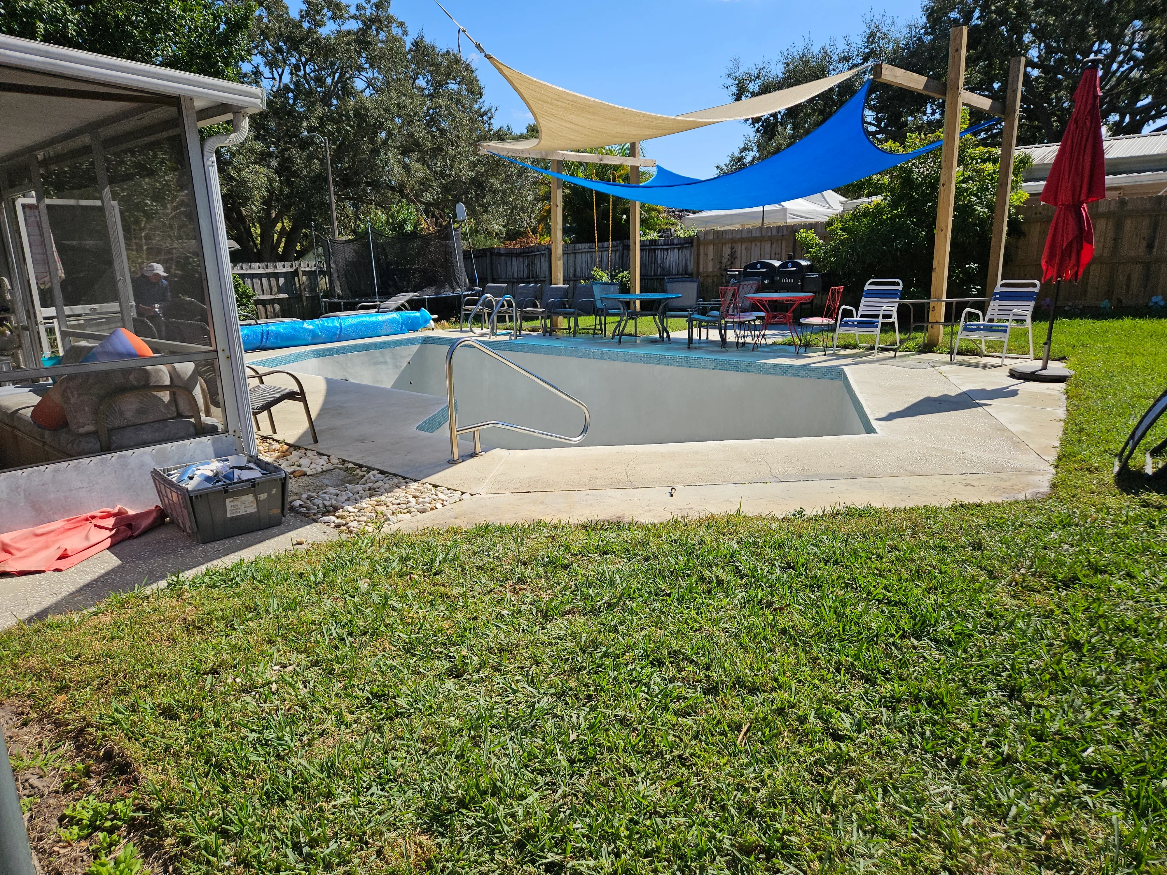 In-ground pool with concrete deck, shade sails, and maintenance equipment during seasonal service