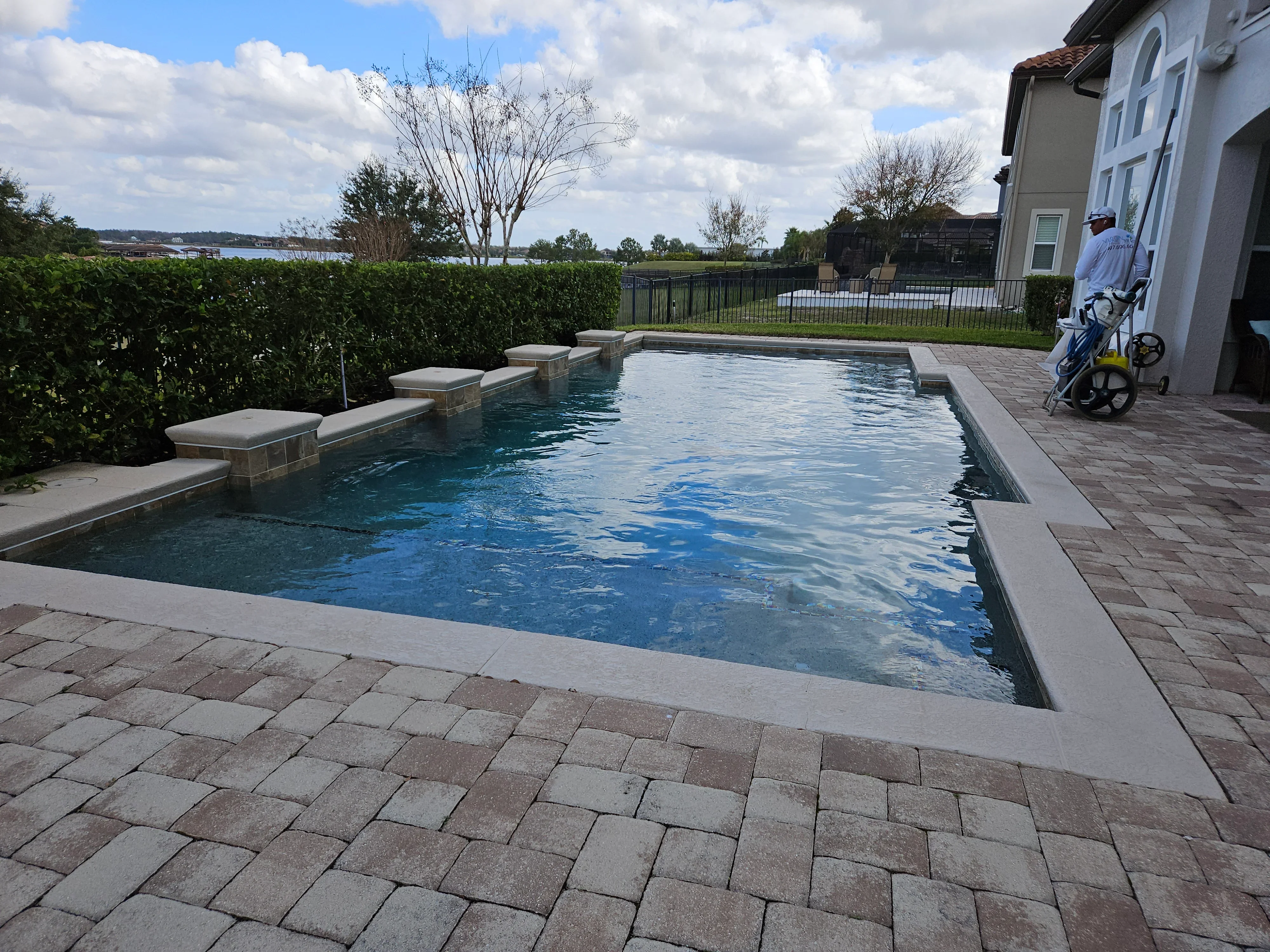 Rectangular pool with stone seating ledges and multi-toned paver deck surrounding residential home