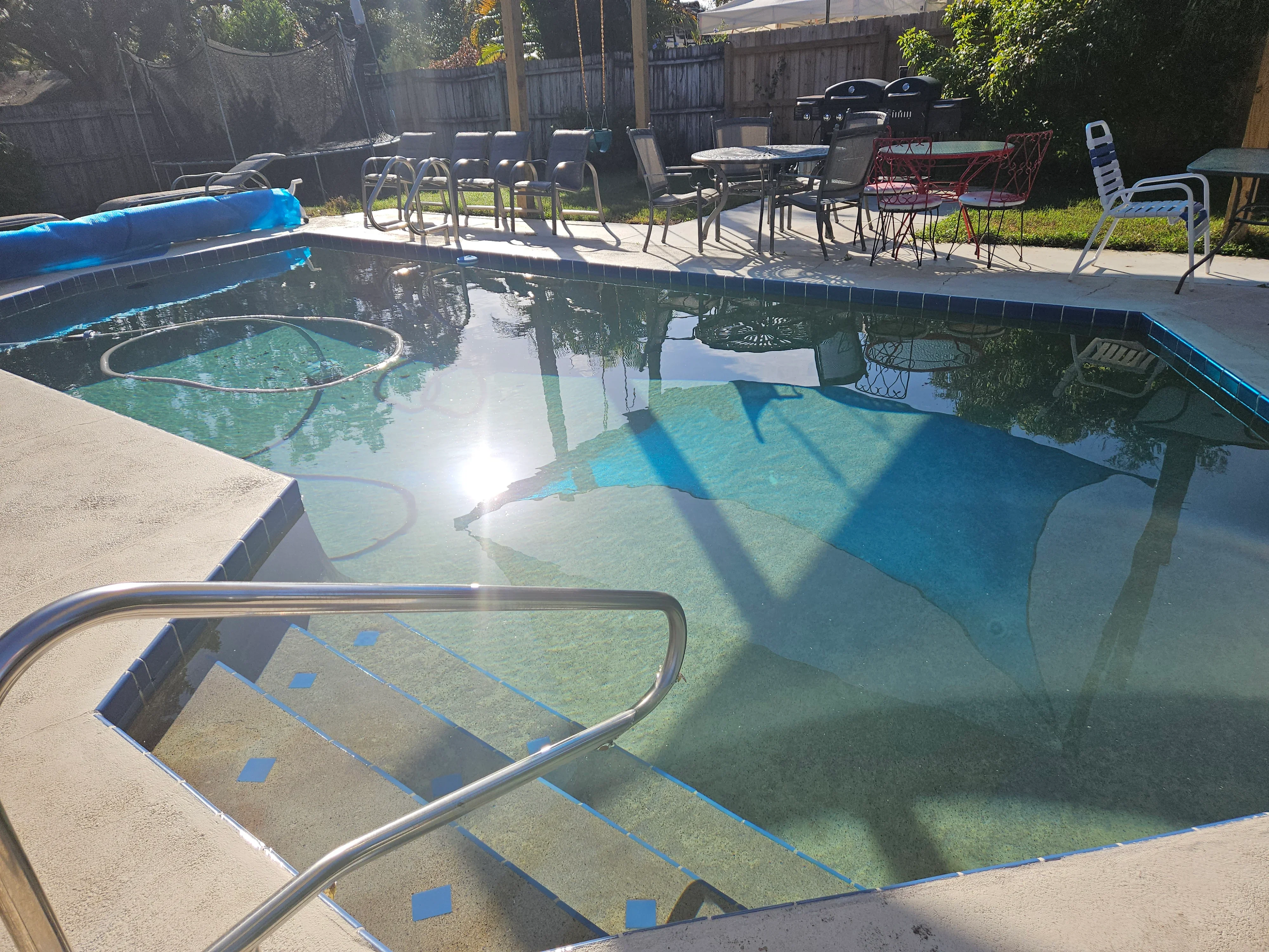 Clear blue residential pool with concrete deck, metal railings, and maintenance equipment visible