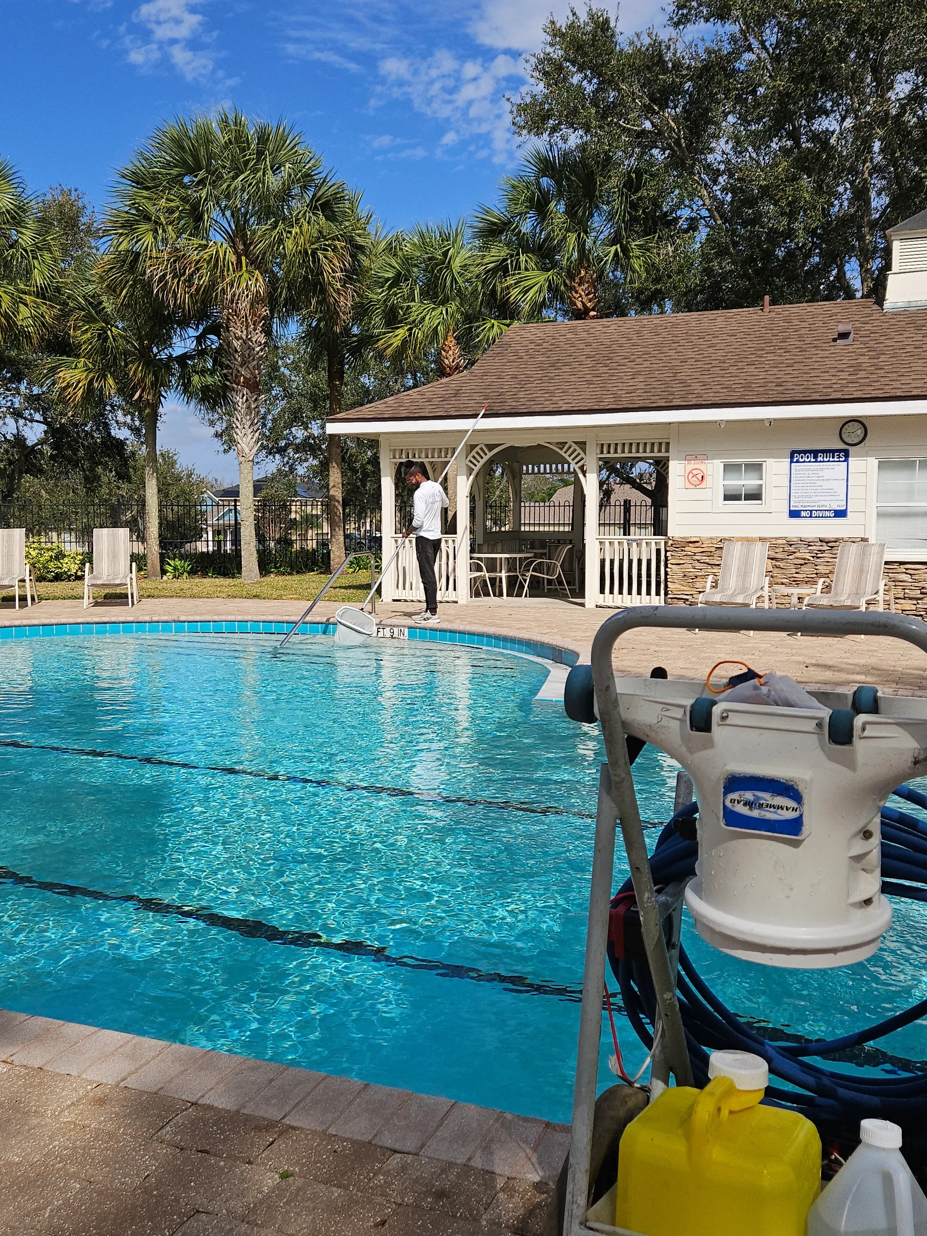 White pool filter tank with pump mounted on wooden deck beside turquoise pool water