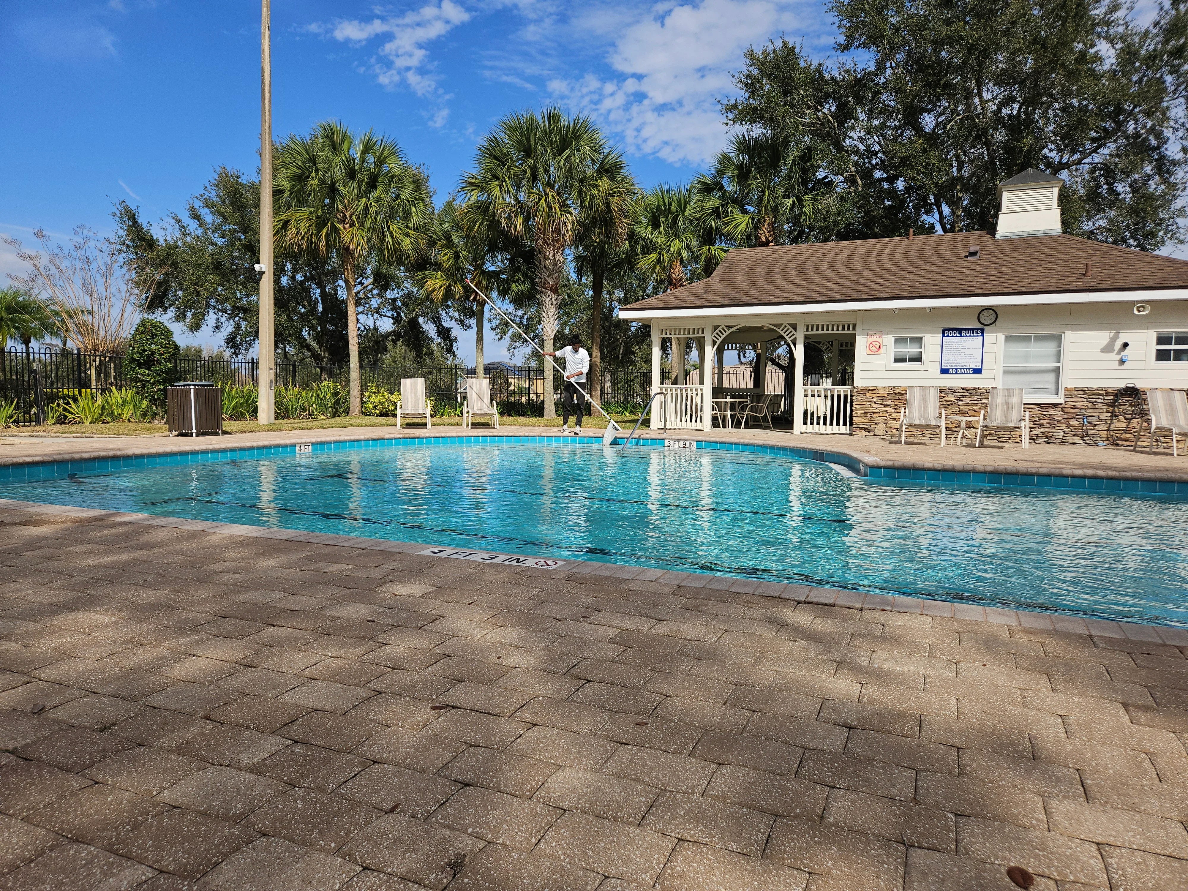Clear blue swimming pool with paver deck and white pool house with stone veneer