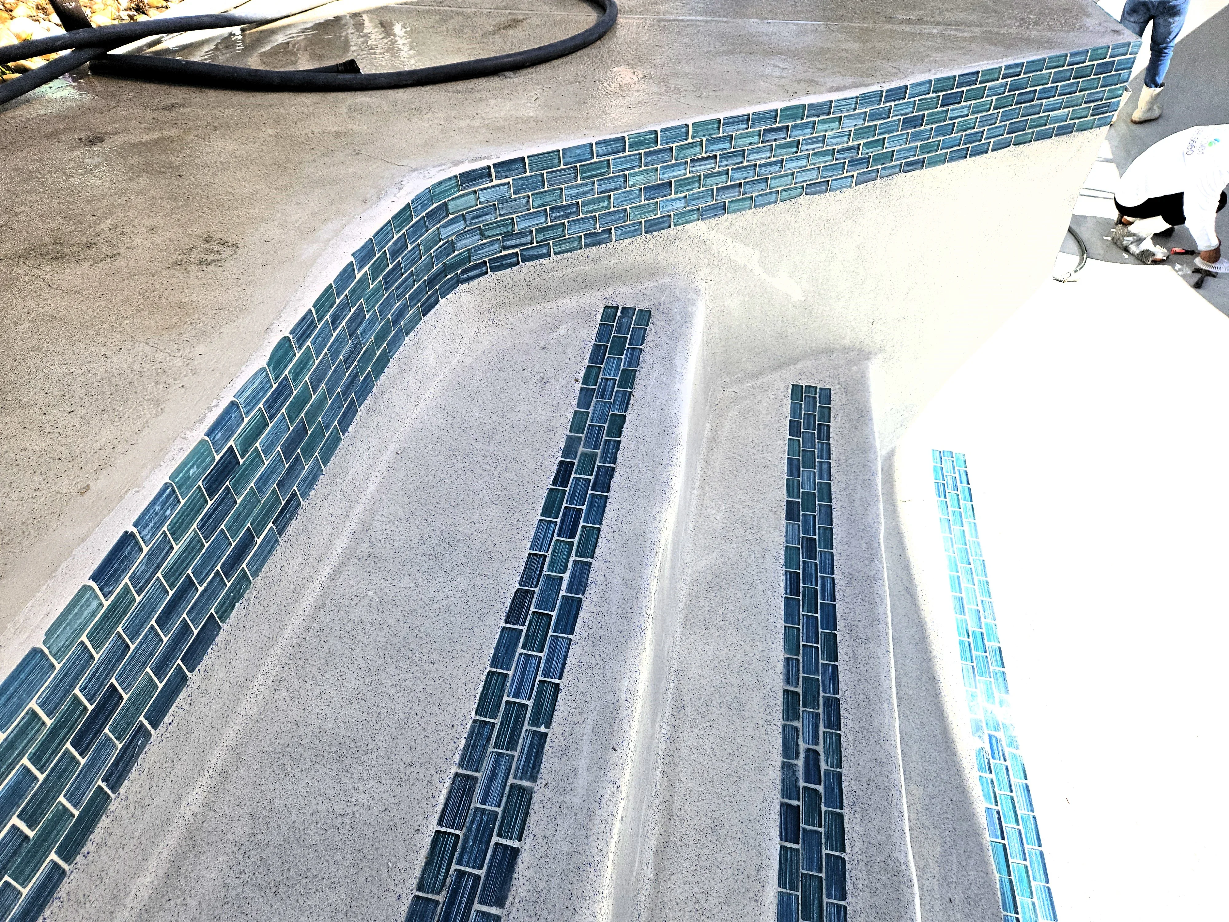 Glass tile installation on pool steps with blue and turquoise tiles in linear pattern