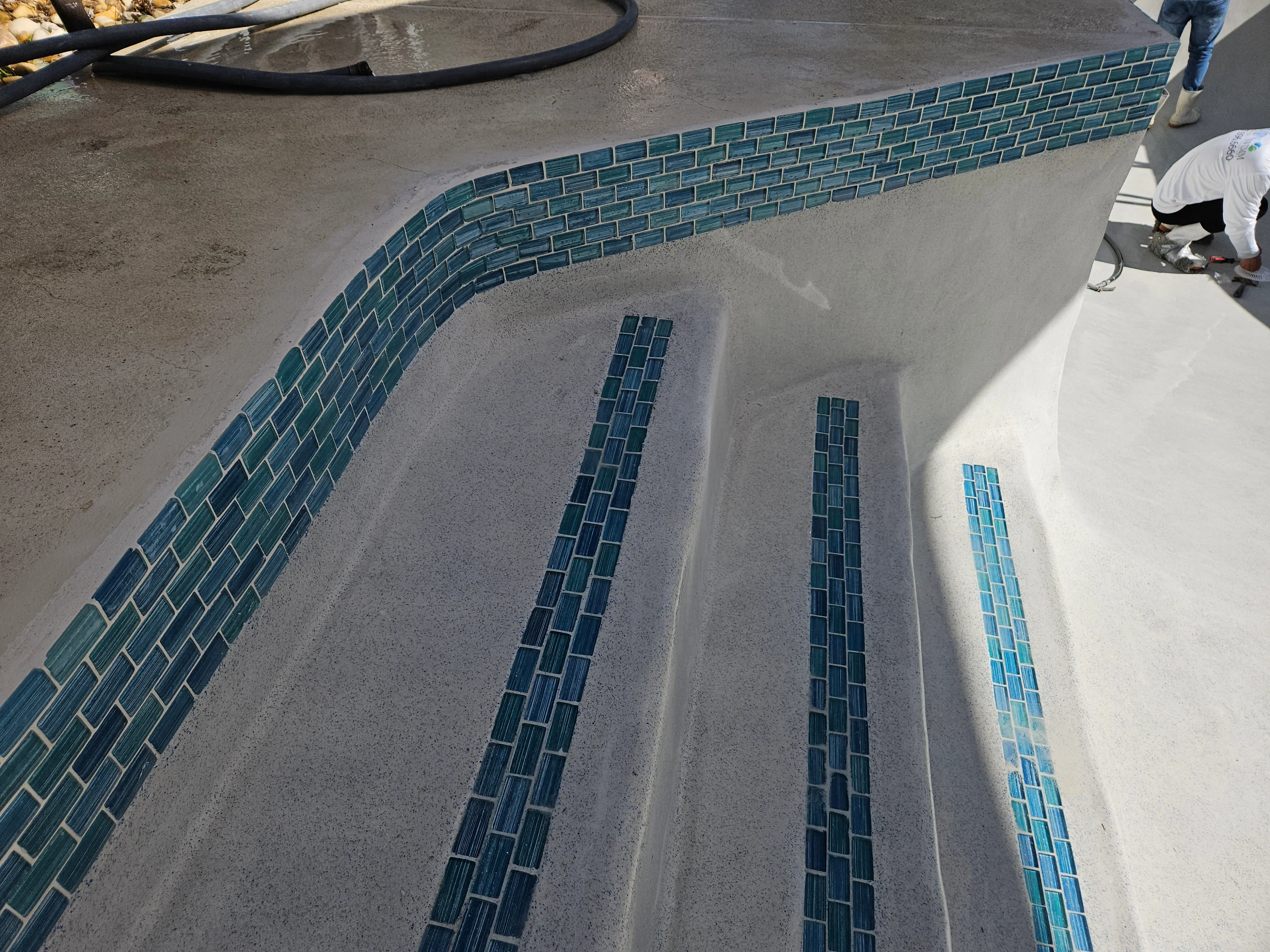 Teal glass subway tiles installed along pool waterline in running bond pattern