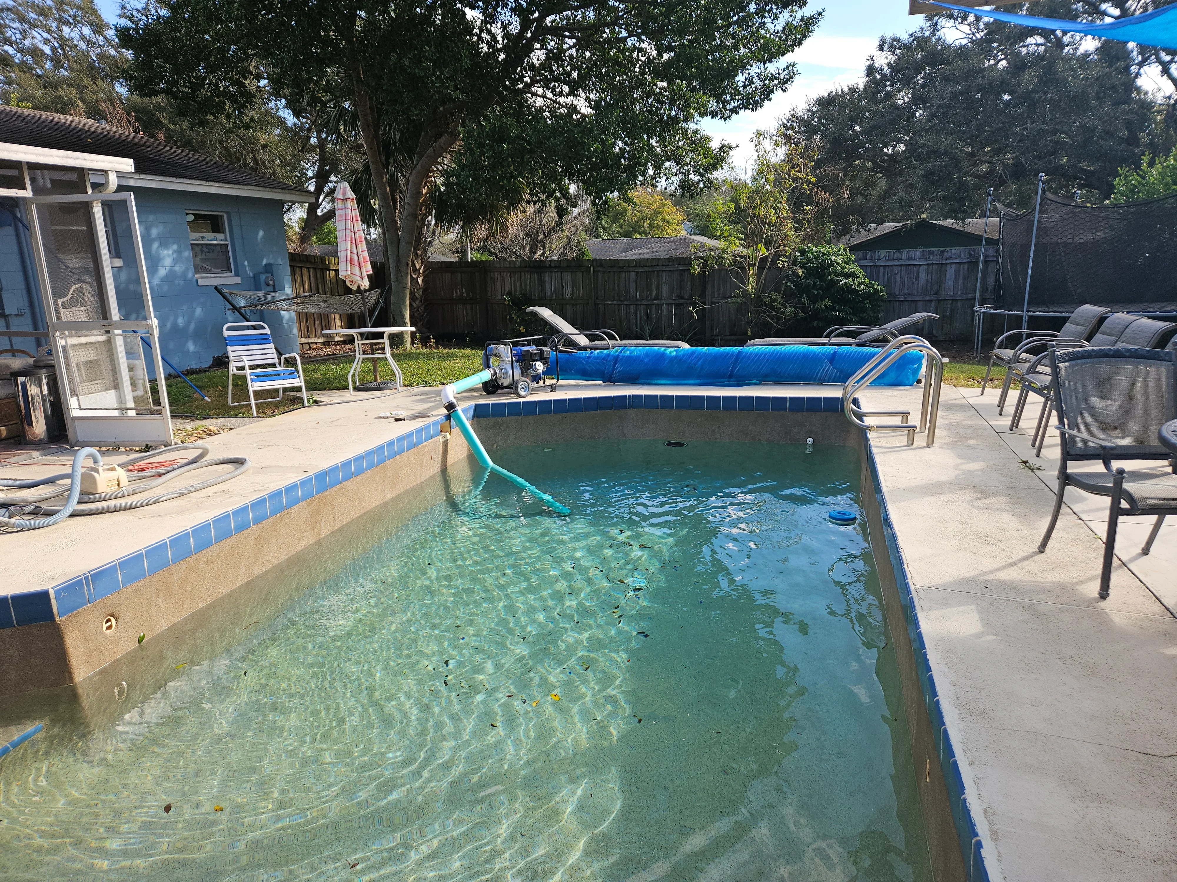Sparkling residential pool with blue tile coping, clear water, concrete deck, and maintenance equipment