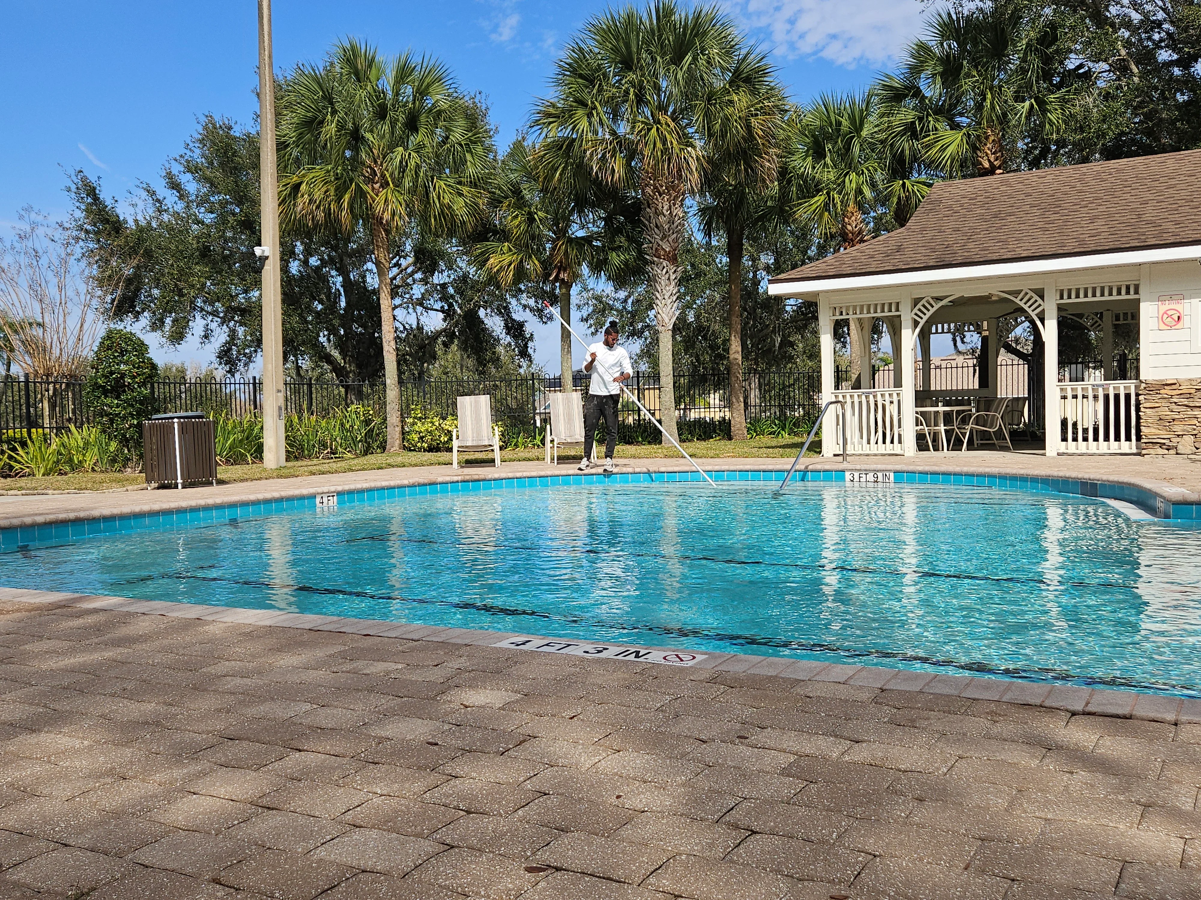 Clean blue commercial pool with concrete deck, white pool house, and iron fencing