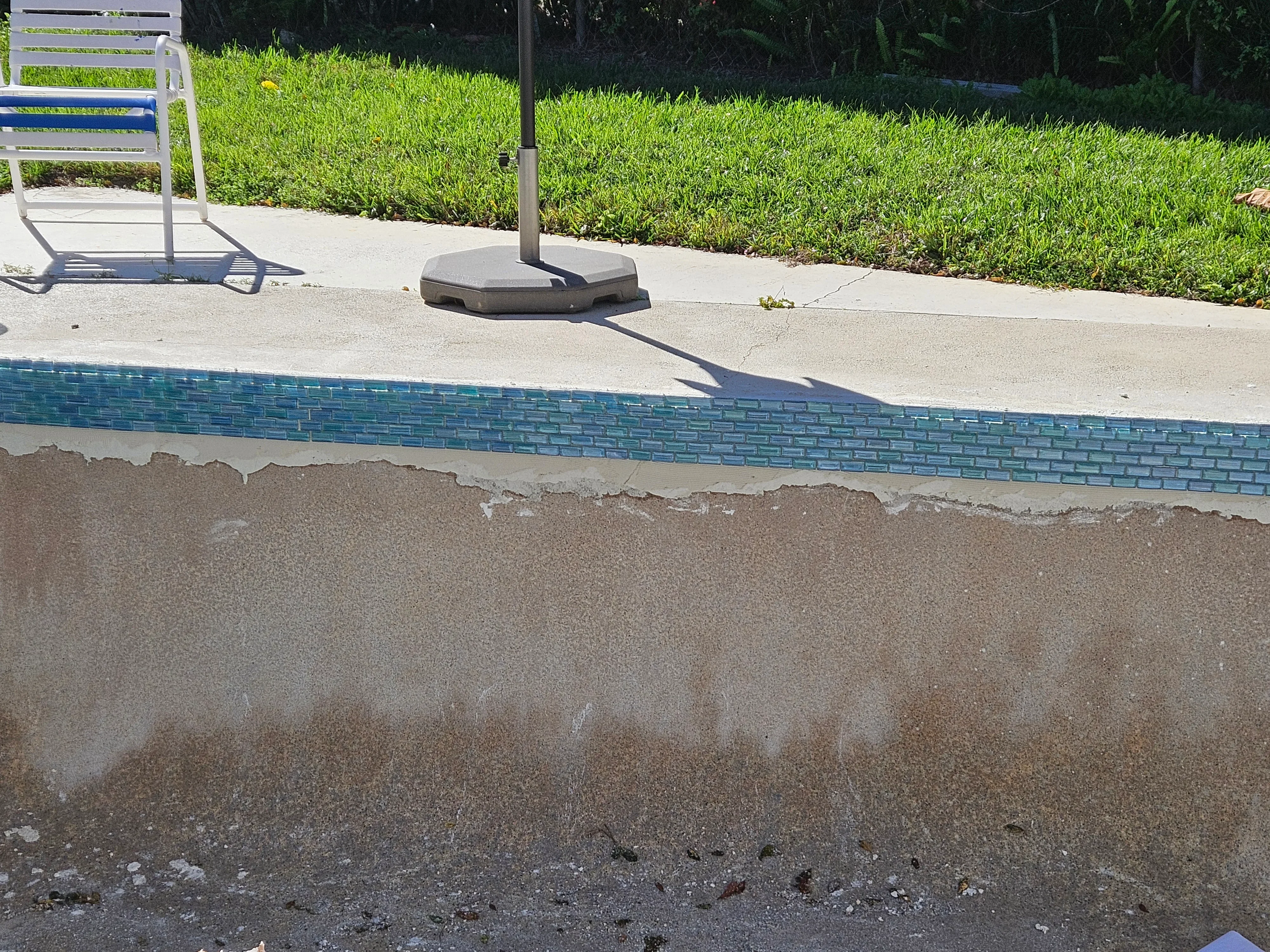Pool waterline with turquoise glass tile border, concrete deck, and sand base layers