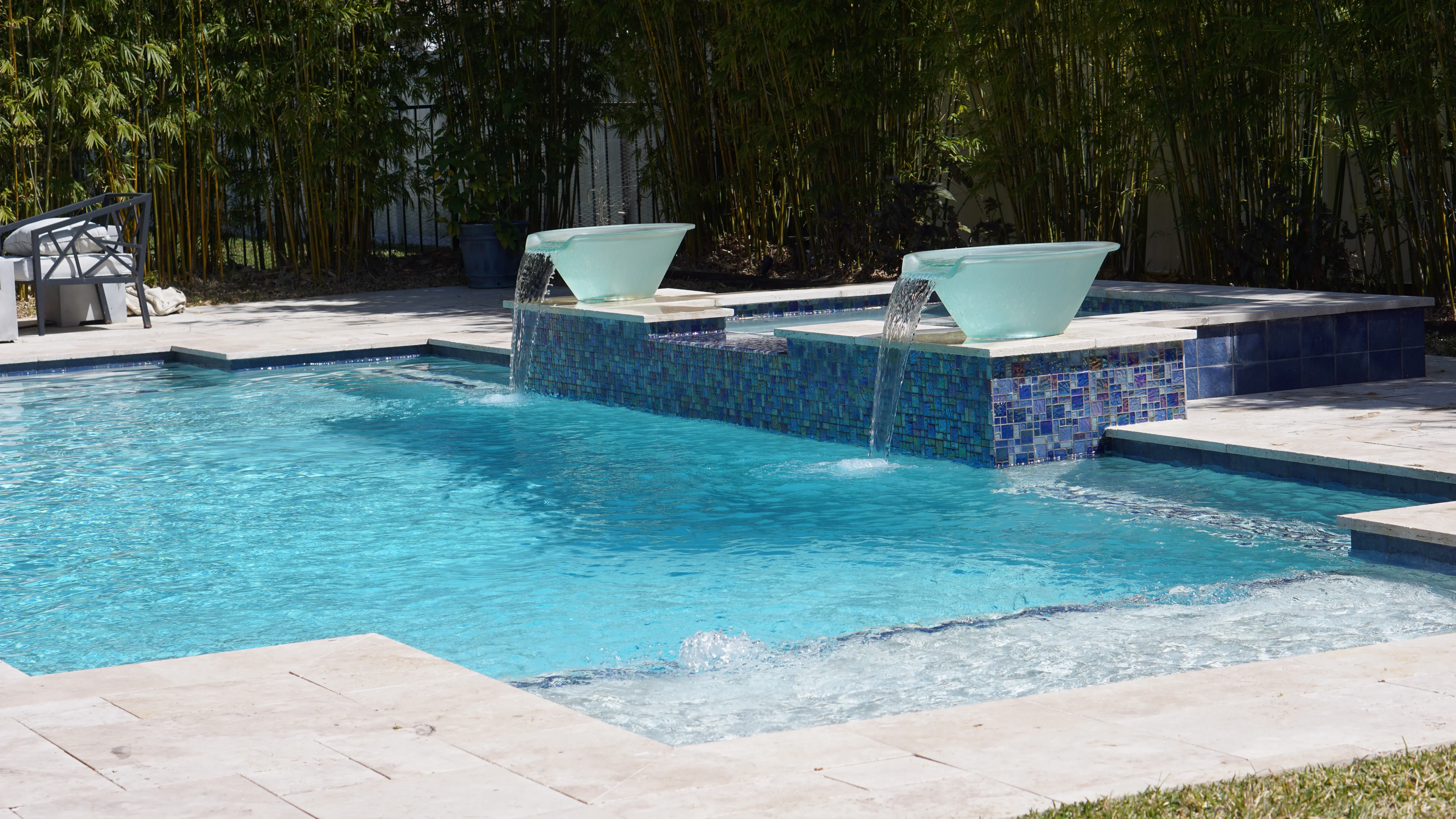 Turquoise pool with dual waterfall features, glass tile work, and concrete deck
